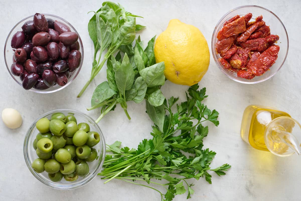 Ingredients for recipe: two types of olives, garlic, fresh parsley and basil, sundried tomatoes, and oil.