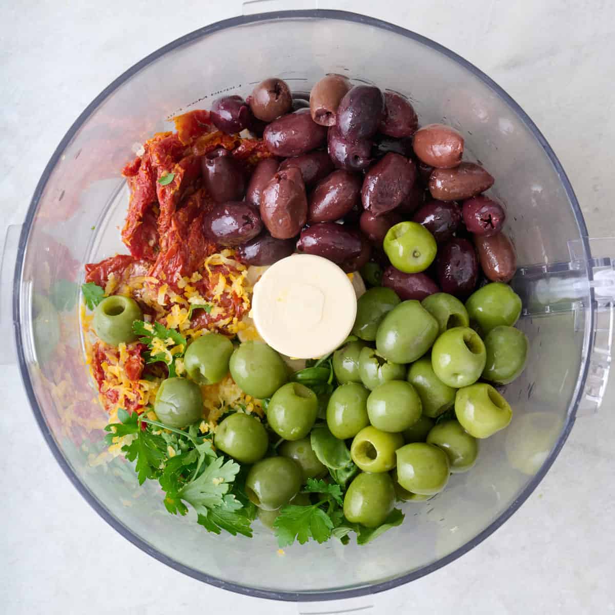 Drained soaked sundried tomatoes in the bowl of a food processor with lemon juice and zest, garlic, olives, parsley, and basil.