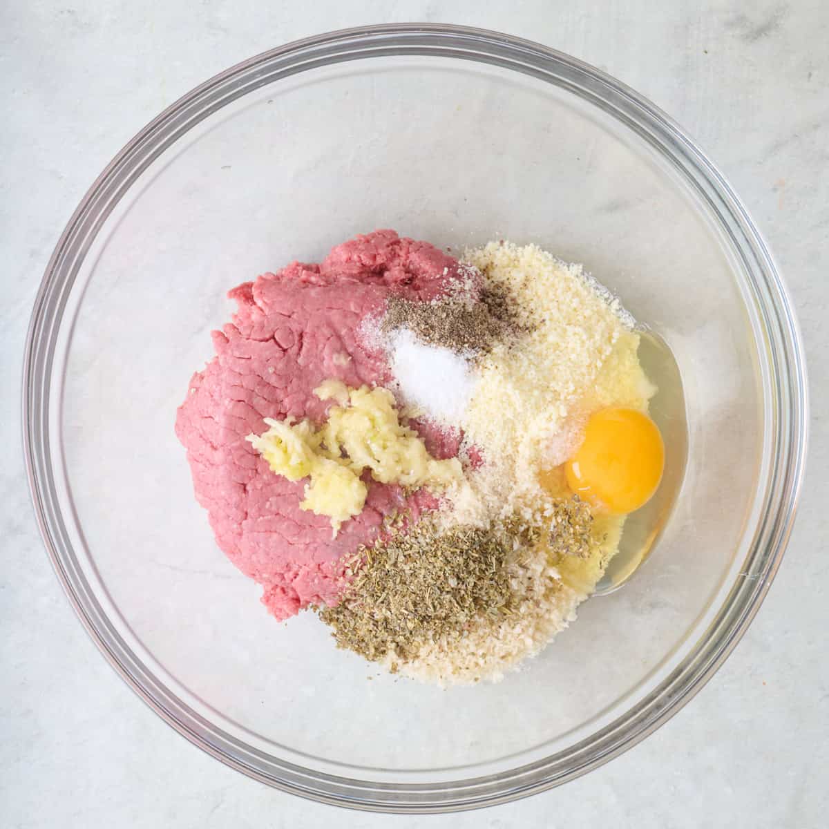 Ground beef, garlic, spices, parmesan, egg, and breadcrumbs in a bowl.
