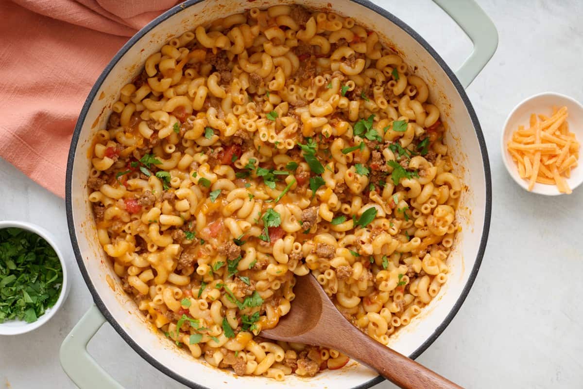 Taco pasta in a pot with a spoon resting on top and ingredients nearby.