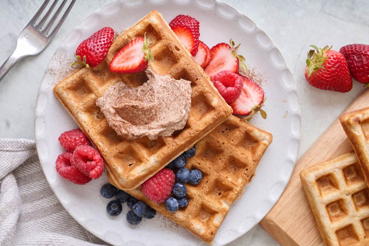 a plate of cinnamon waffles with toppings and more ingredients nearby.