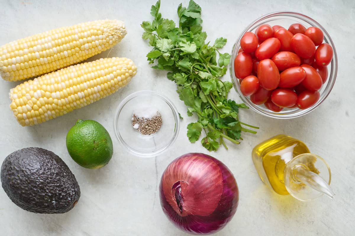 Ingredients for corn tomato avocado salad: corn, avocado, red onion, lime, cilantro, tomatoes, olive oil, salt, and pepper.