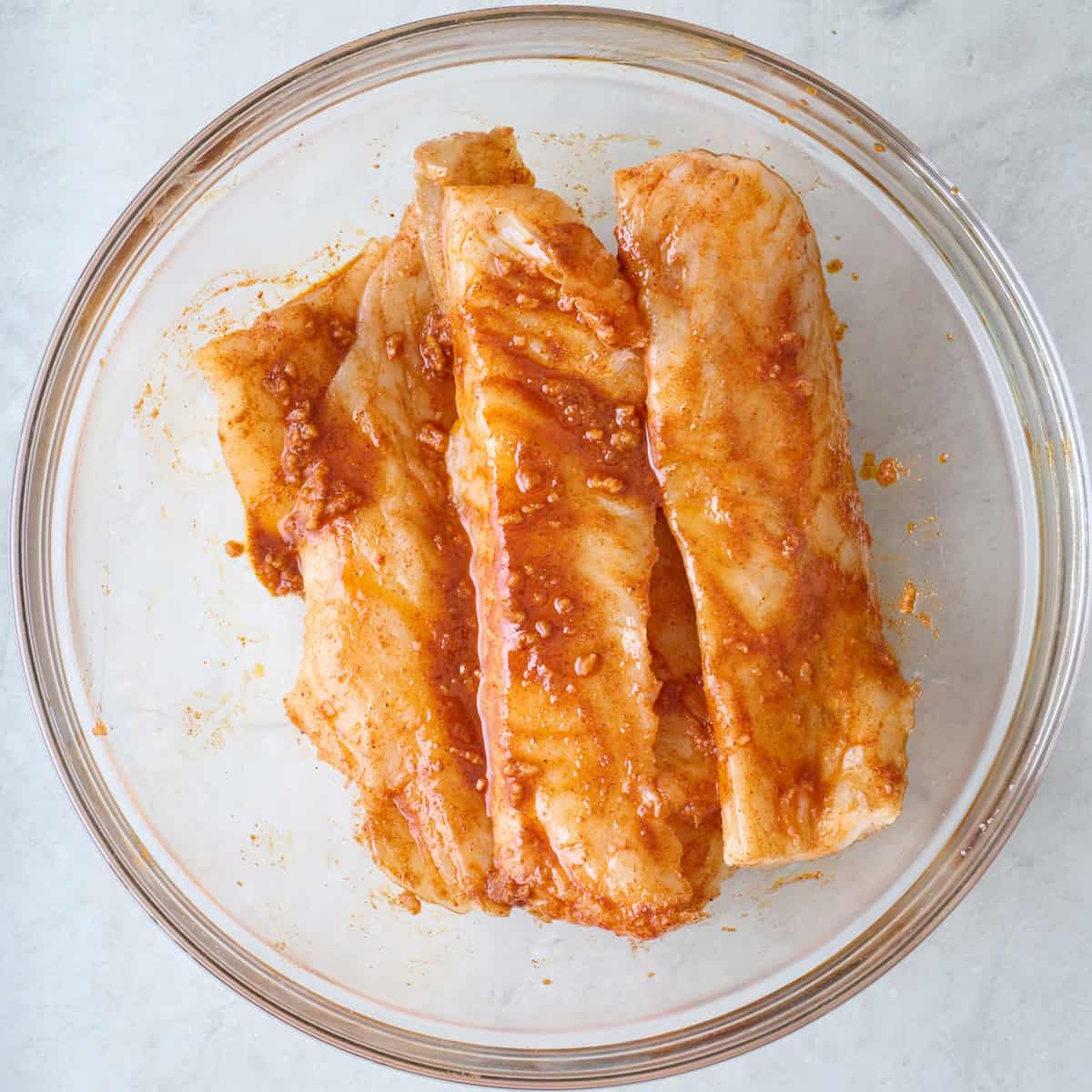 Marinaded white fish fillets in a large glass bowl.