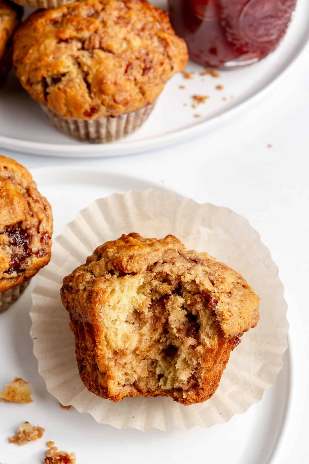 Peanut butter and jam muffin on a small plate with a bite taken out and more muffins nearby.
