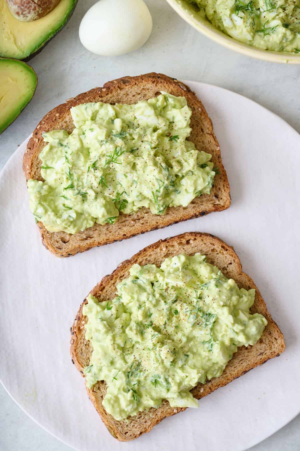 Open-faced avocado egg salad sandwich on multi-grain bread.