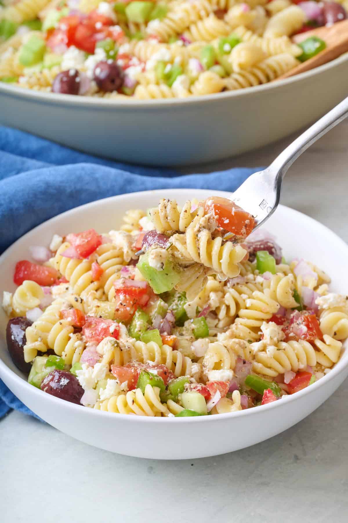 Fork lifting up a bite of Greek pasta salad from a bowl.