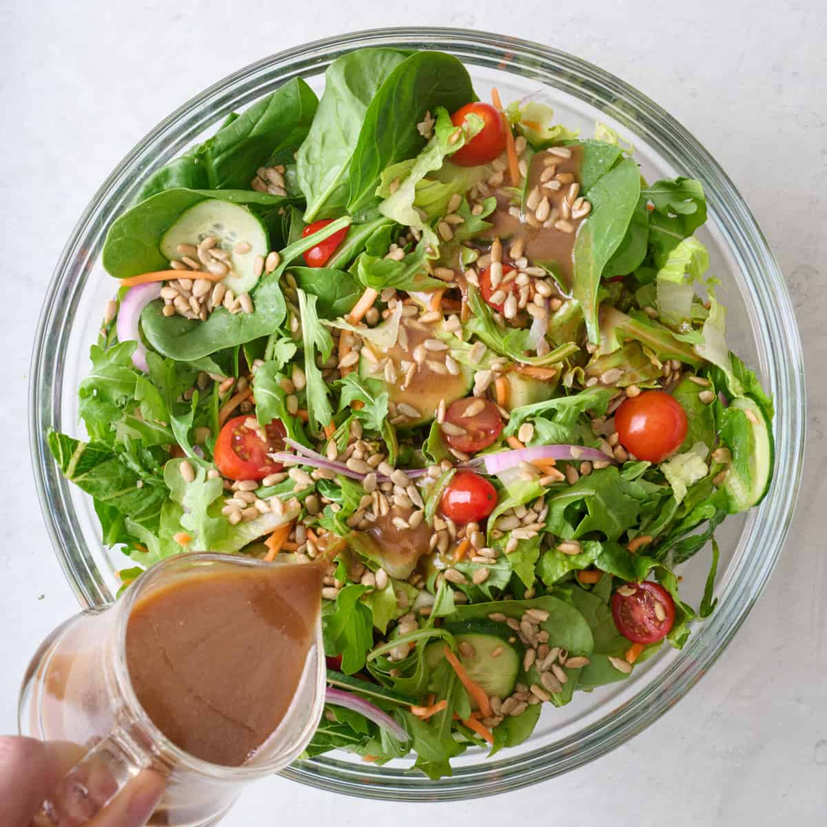 Dressing being poured onto a mixed green salad.