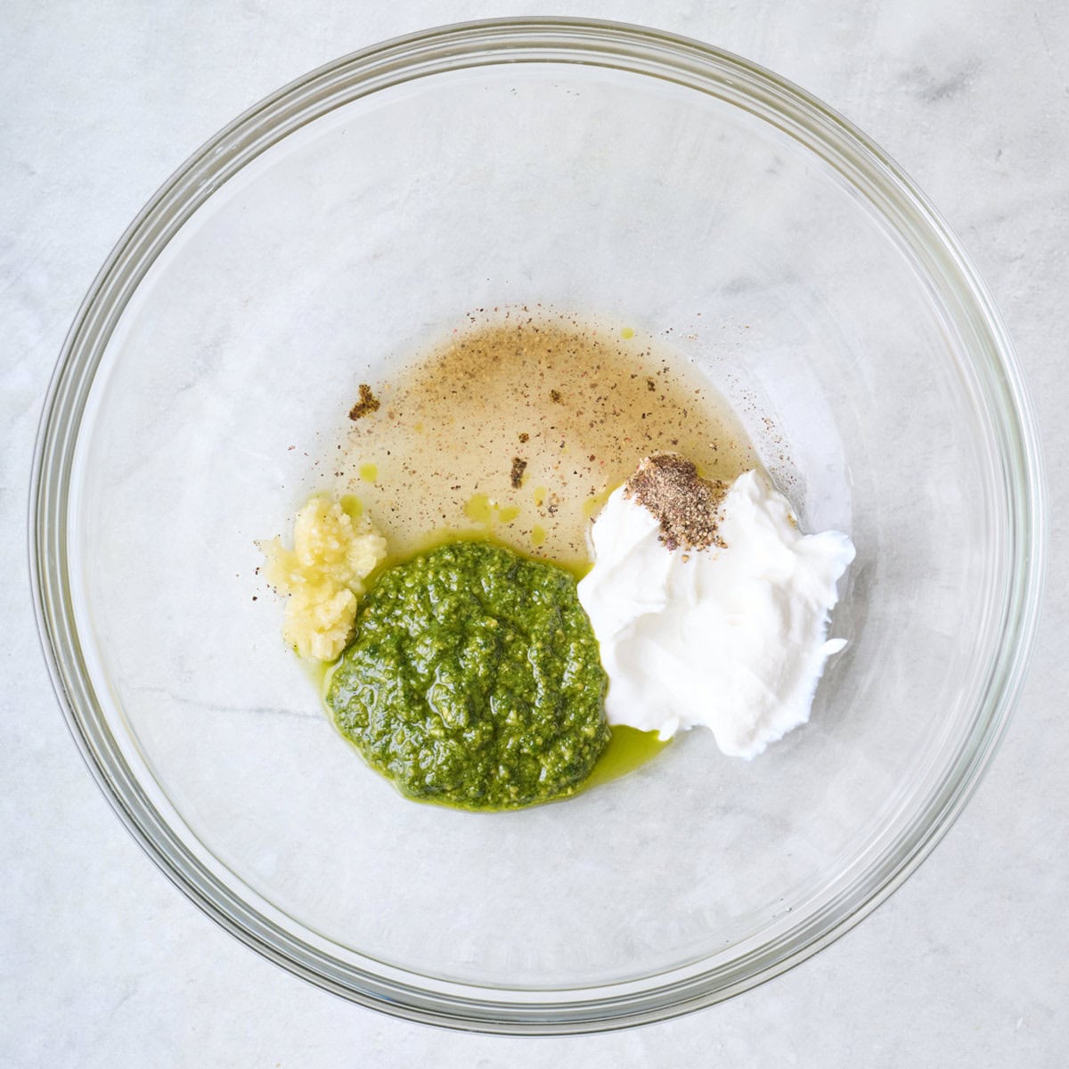 Pesto, yogurt, oil, garlic, and seasonings in a bowl before mixing.