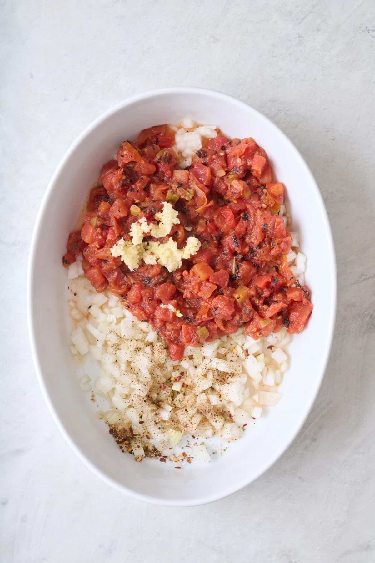 Onions, garlic, tomatoes, salt, pepper, and crushed red pepper in oval baking dish.