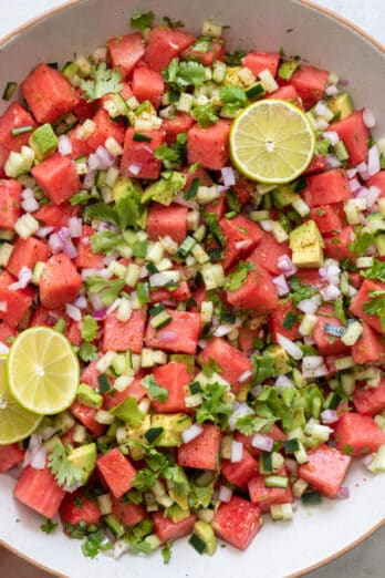 Large bowl of the watermelon salsa garnished with cilantro and lime slices with small bowl or tortilla chips to the side.
