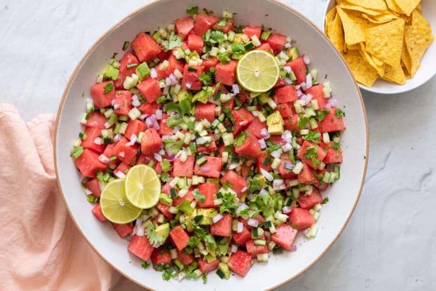 Large bowl of the watermelon salsa garnished with cilantro and lime slices with small bowl or tortilla chips to the side.