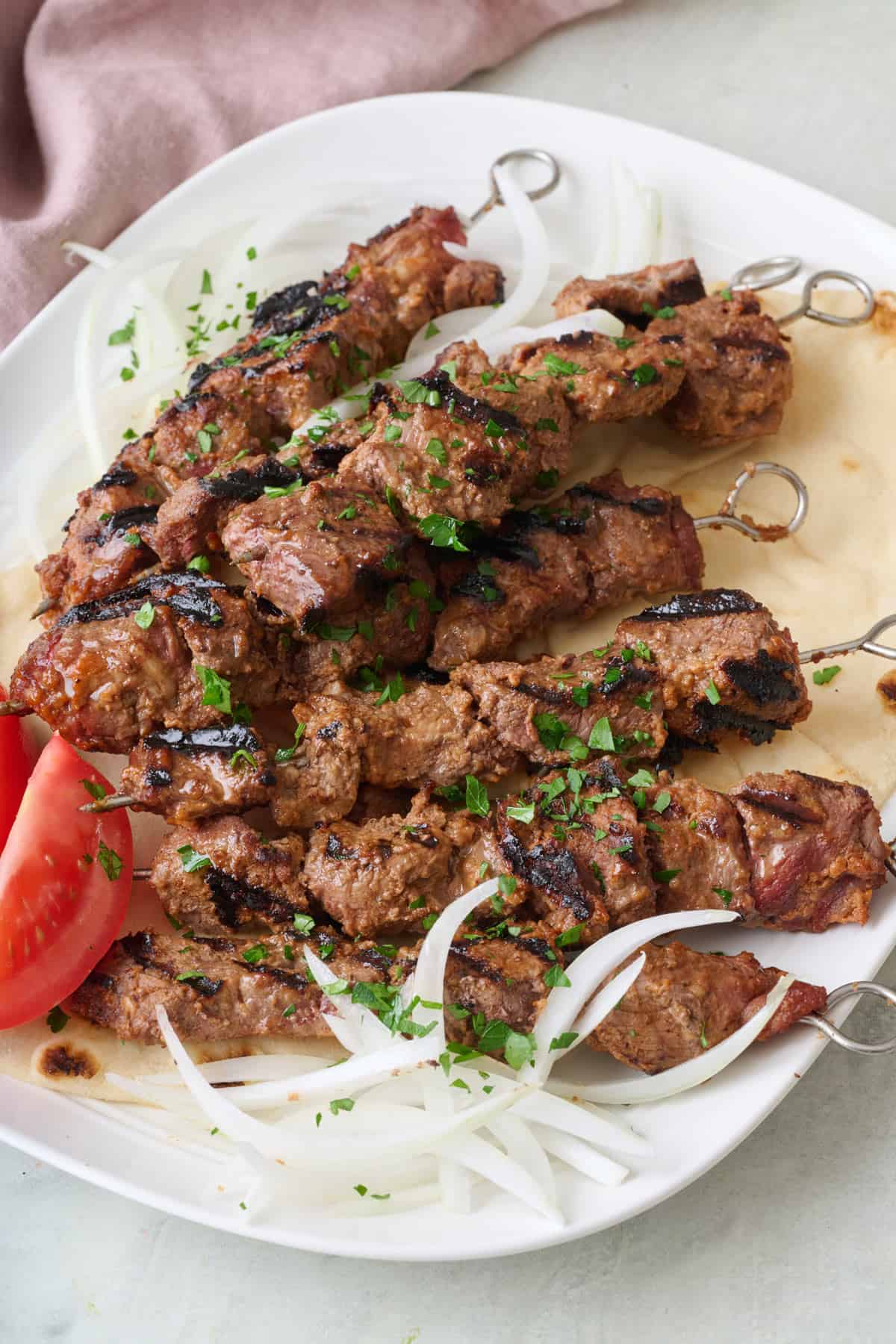 West African beef skewers on a large pita served on a platter with onions and tomatoes.
