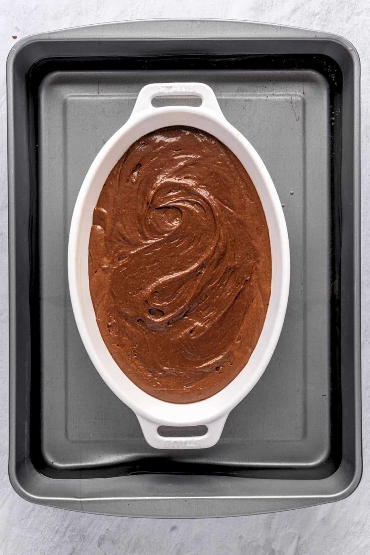Brownie pudding batter in the prepared baking dish that is sitting in a large baking pan filled with water.