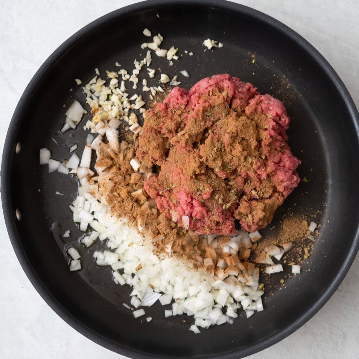 Oil, onions, ground beef, and garlic in a skillet seasoned with oregano, cinnamon, salt and pepper before mixing.