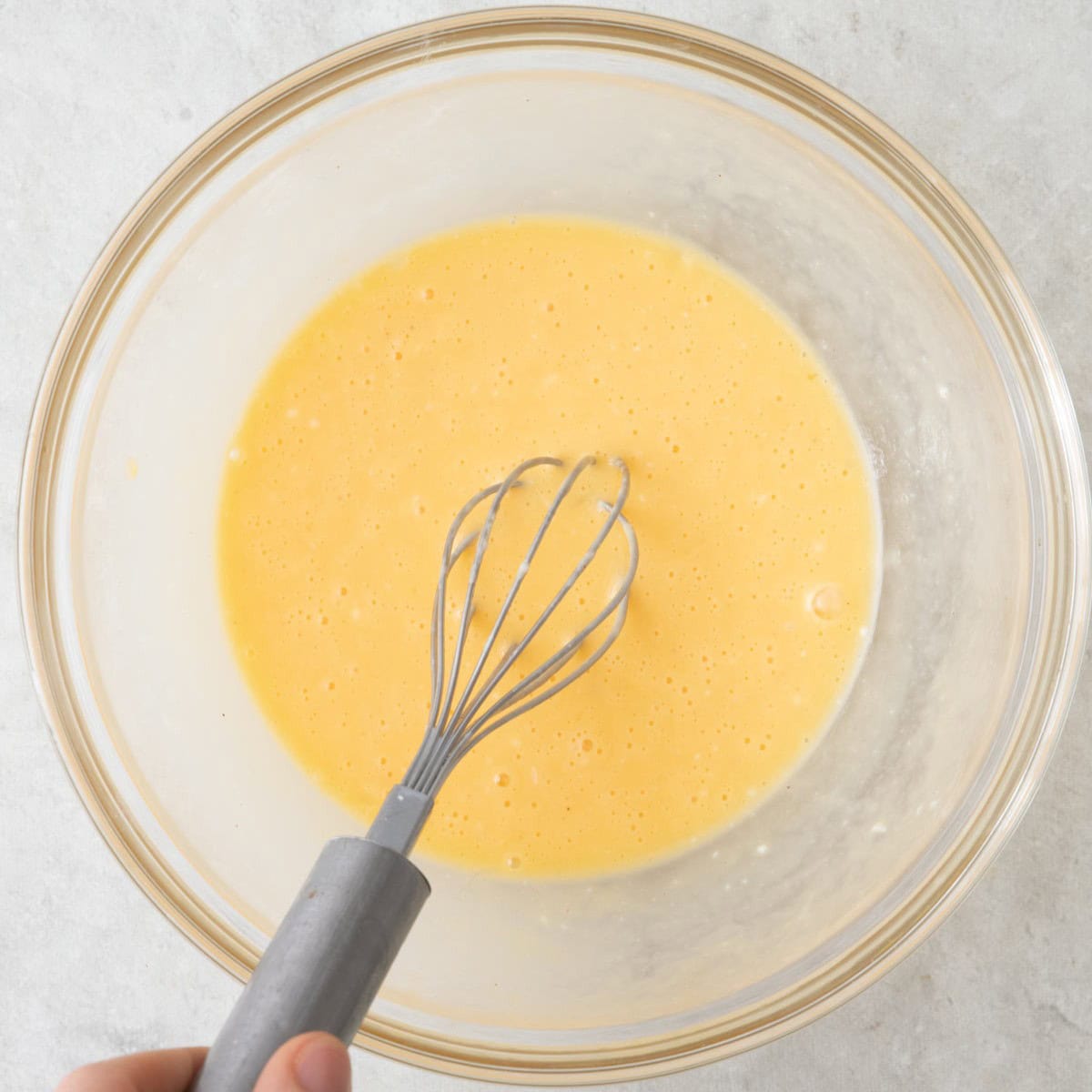 Beaten eggs in a bowl with 2 tablespoons bechamel sauce added with whisk in bowl.