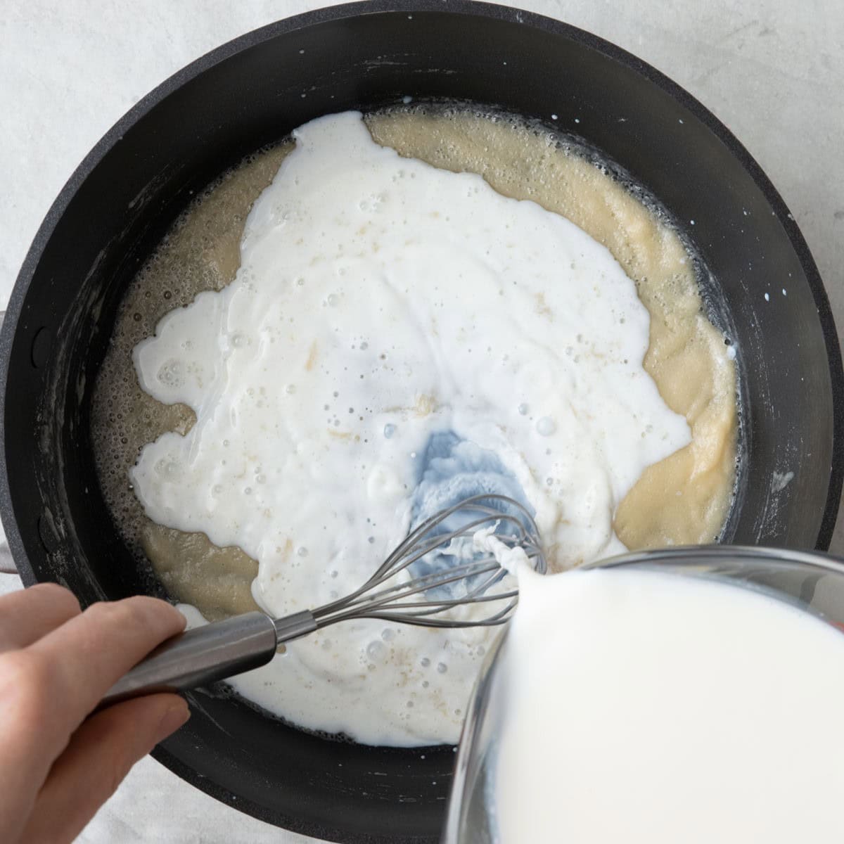 Milk slowing being poured into pan while stirring.