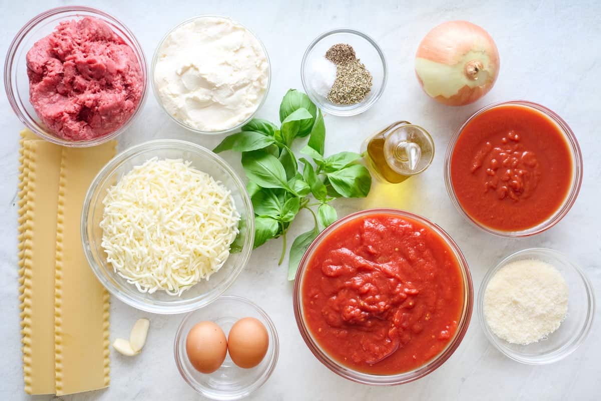 Ingredients for recipe: lasagna sheets, ground beef, shredded cheese, ricotta, fresh basil, garlic, eggs, seasonings, oil, crushed tomatoes, tomato sauce, grated parmesan, and onion.