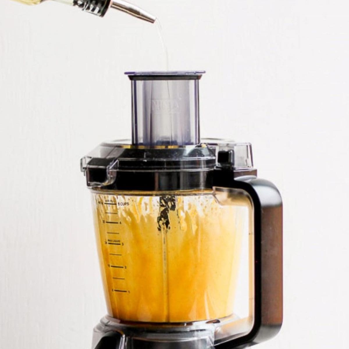 Food processor on with oil being poured in.