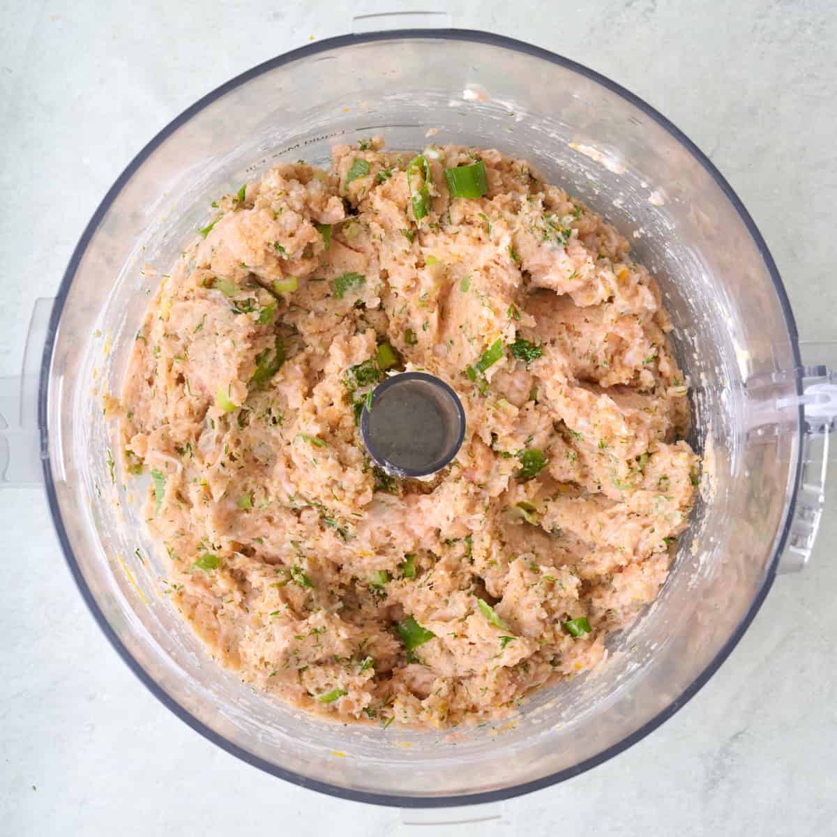Salmon burger mixture in the bowl of a food processor.