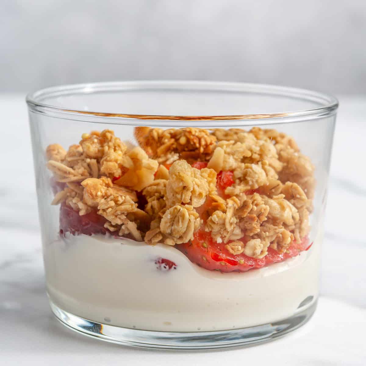 Cream-cheese yogurt mixture, sliced strawberries, and granola in a serving glass.
