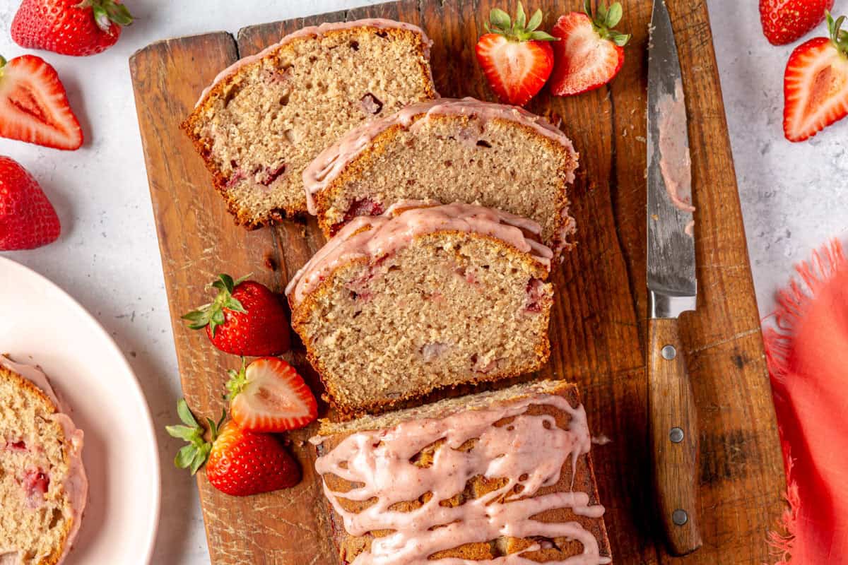 Strawberry Pound Cake loaf with slices cut out laying on a cutting board with other ingredients nearby.