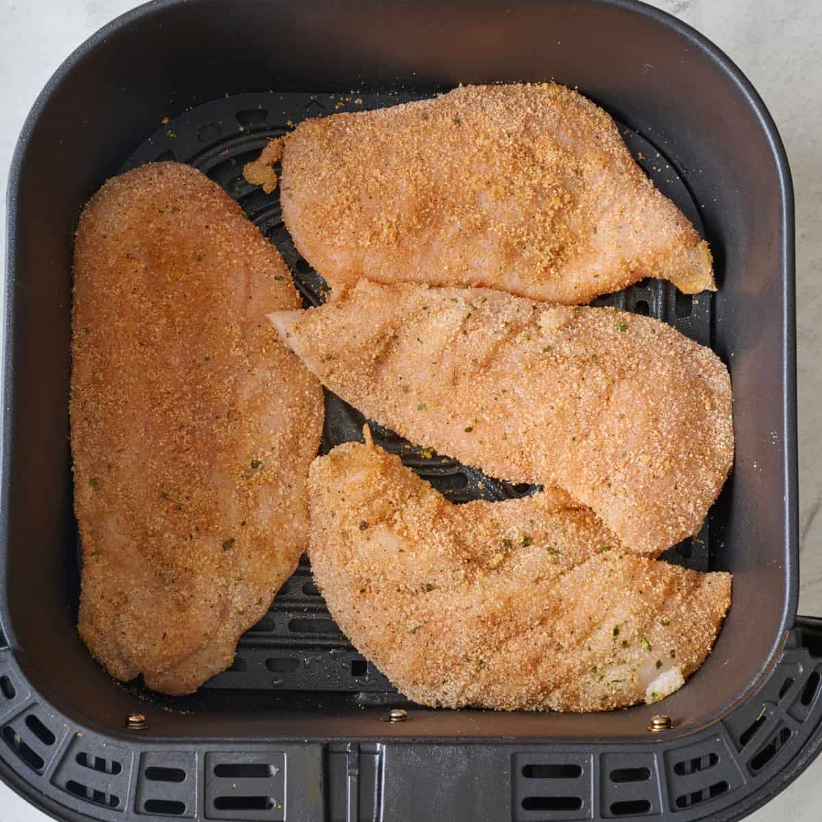 Breaded chicken in an air fryer basket before cooking.
