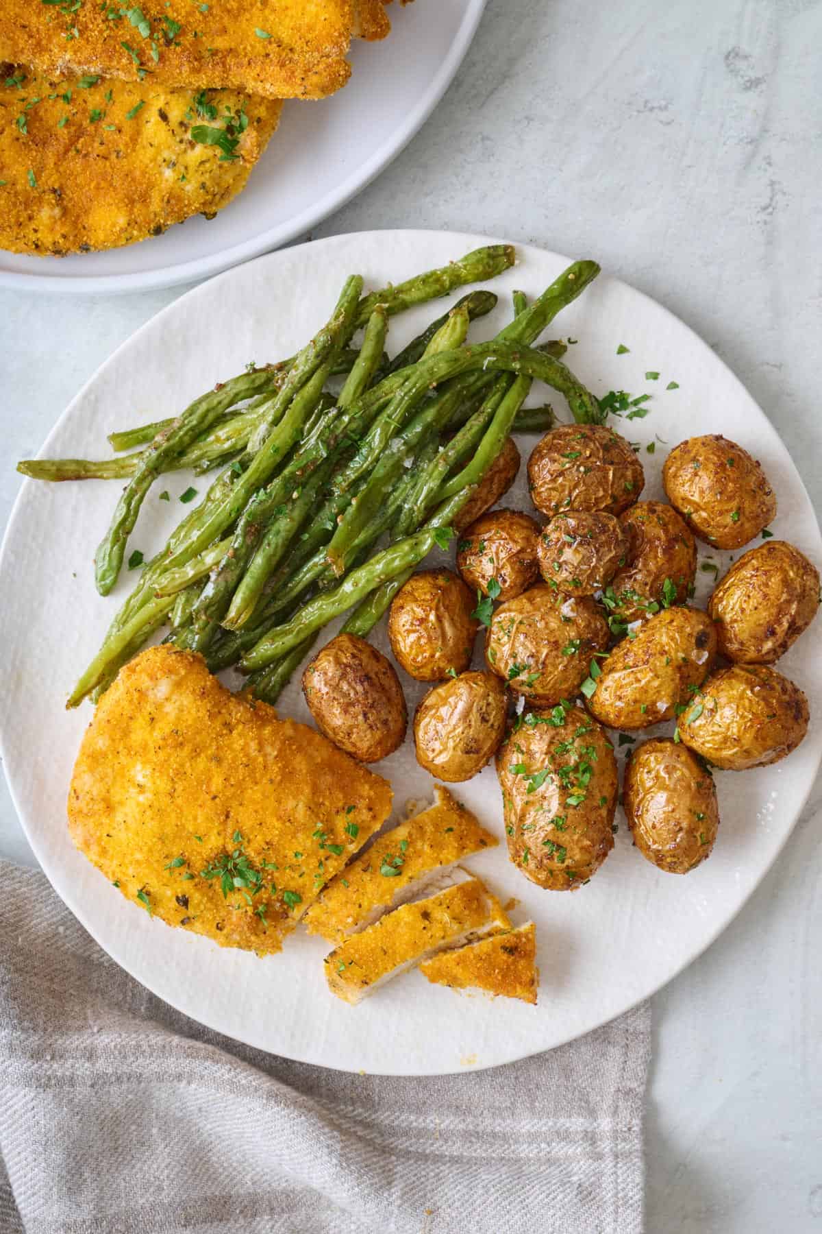 Air fried breaded chicken on a plate with baby potatoes and green beans.