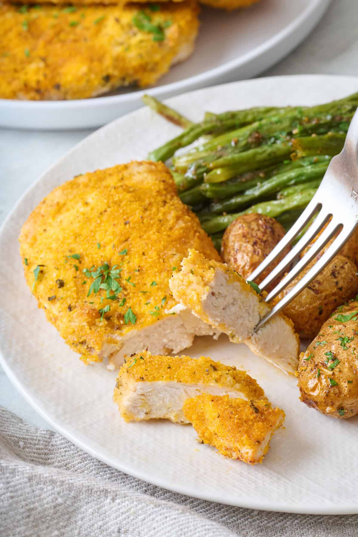 Fork lifting up a piece of breaded chicken from plate.