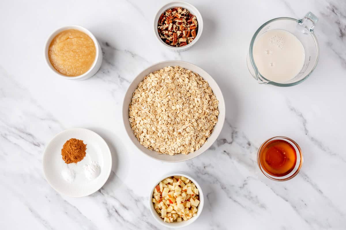 Ingredients for recipe in individual containers: applesauce, cinnamon, pecans, oats, chopped apple pieces, maple syrup, and milk.