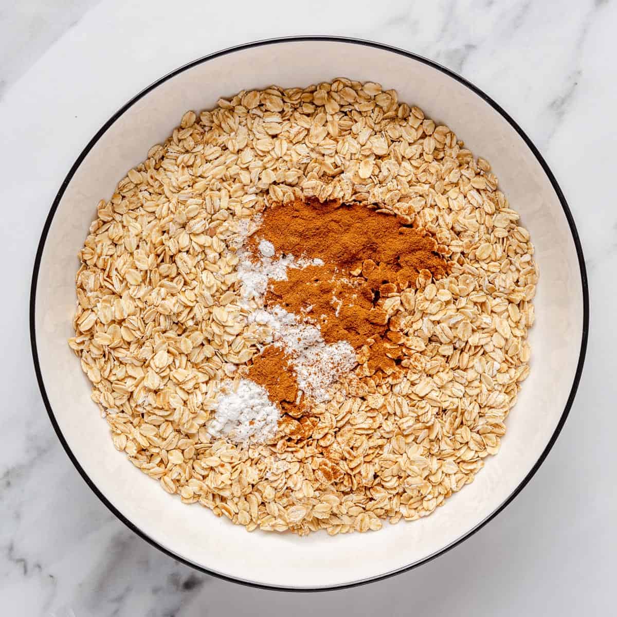 Oats in a bowl with baking powder, salt and cinnamon on top.