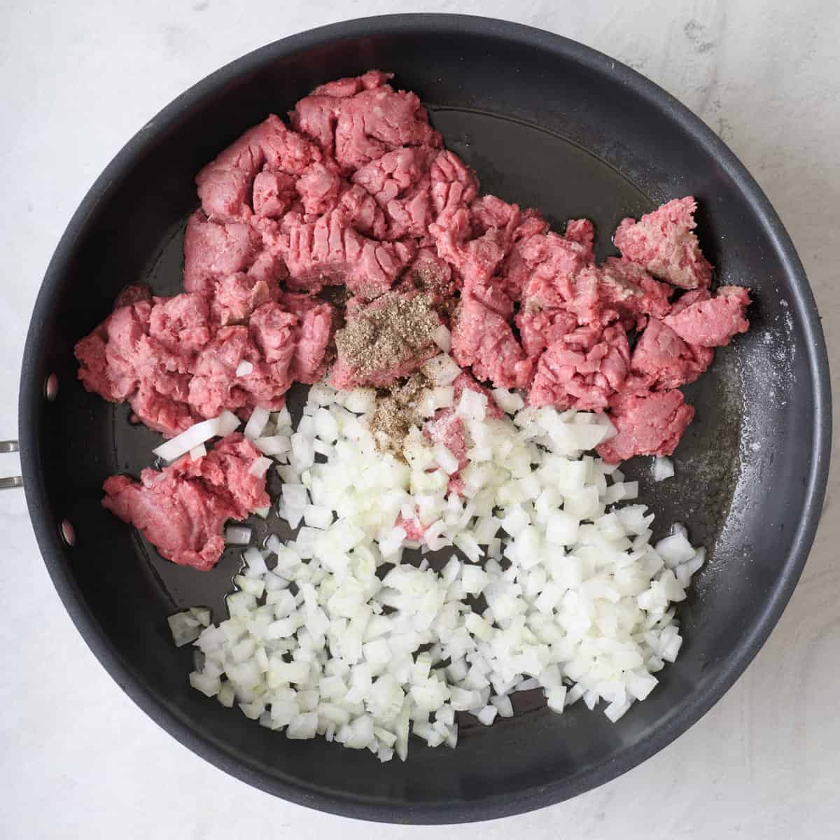 Ground beef and chopped onions in a skillet.