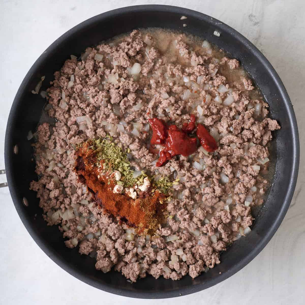Cooked ground beef, spices, and tomato paste in a skillet.