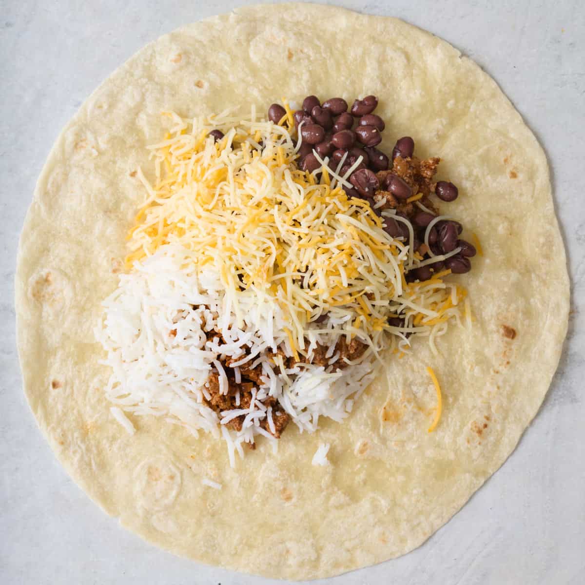 Ground beef, grated cheese, and rice on a tortilla.