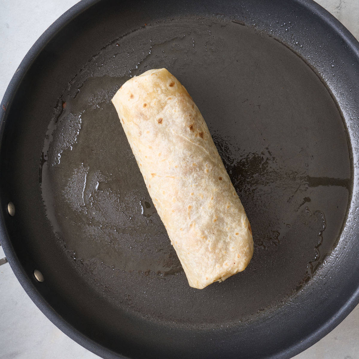 A burrito cooking in a skillet.