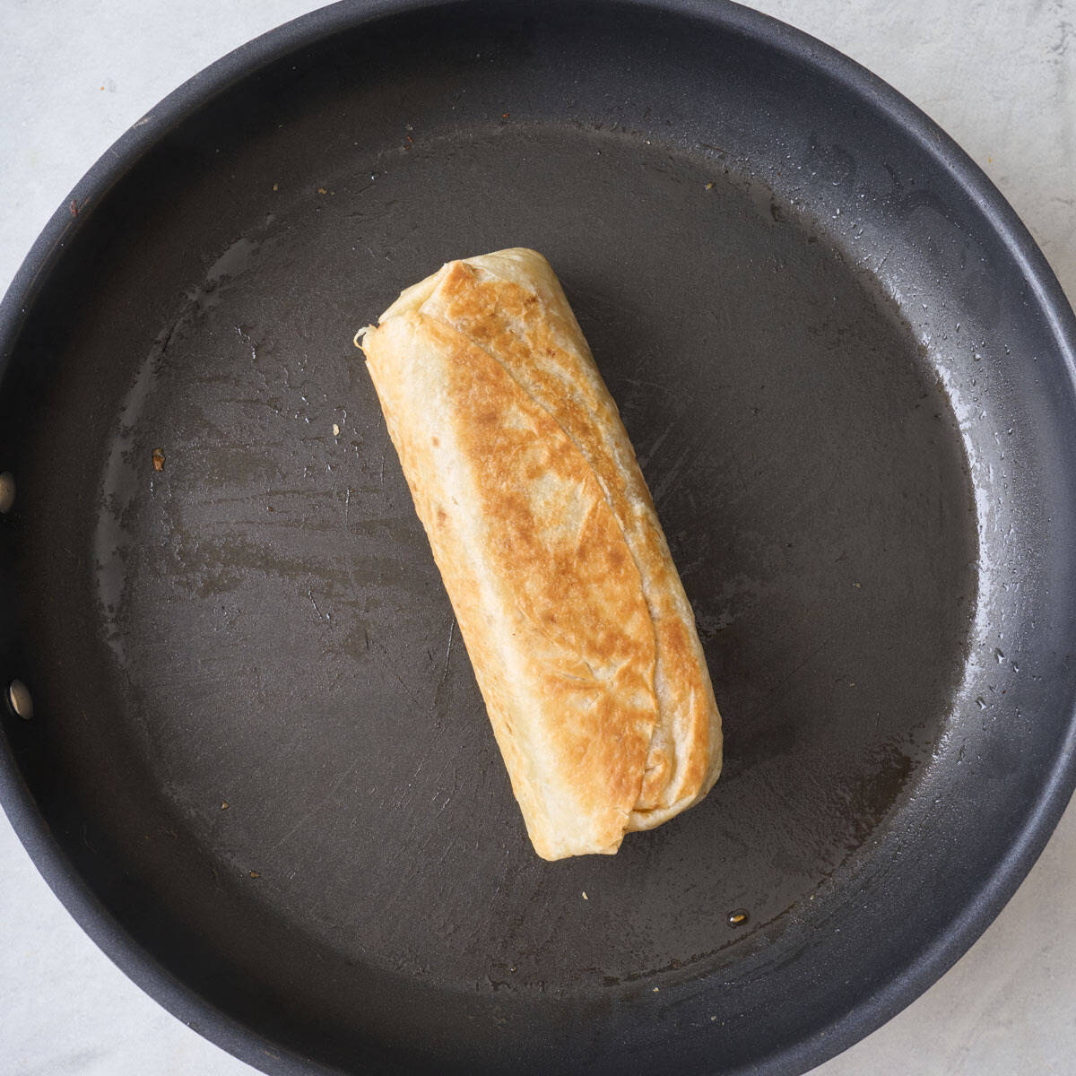 A well-browned burrito in a skillet.