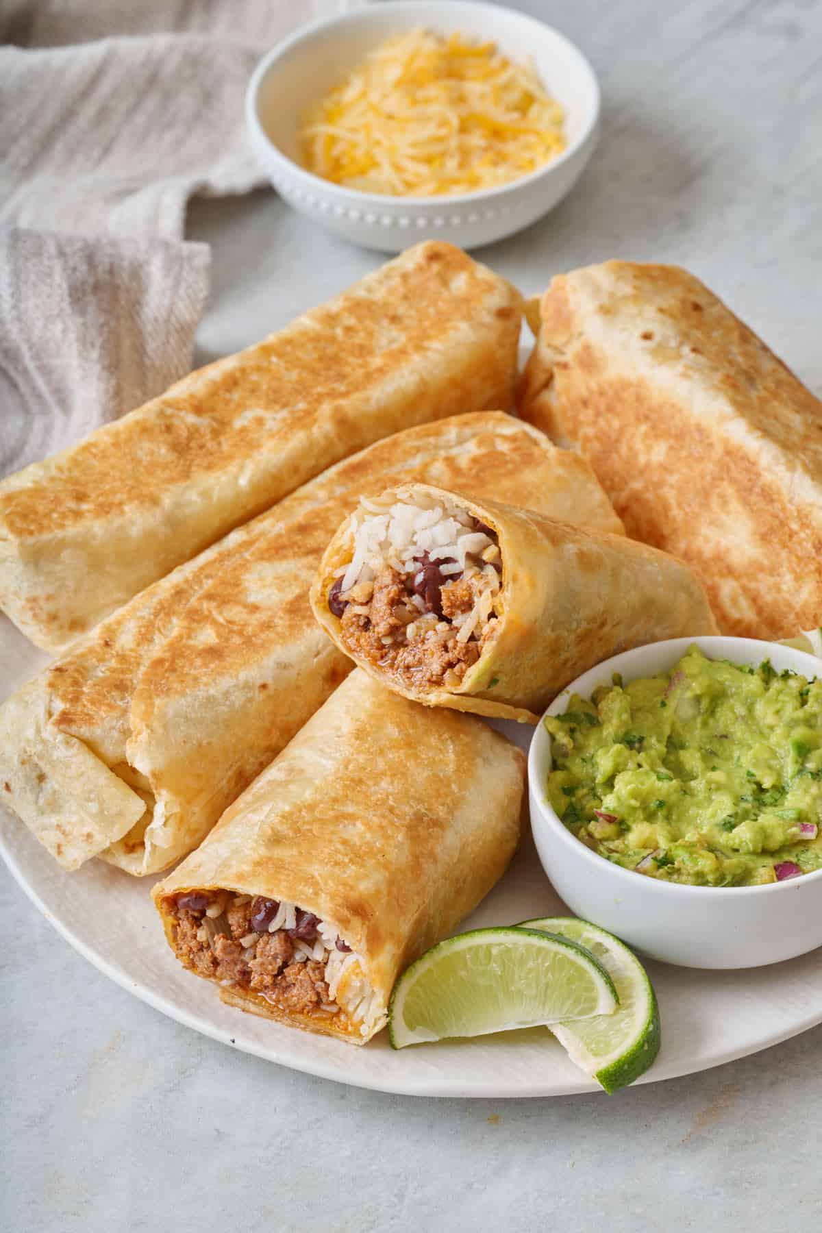 A plate of ground beef burritos with a bowl of guacamole on the side.