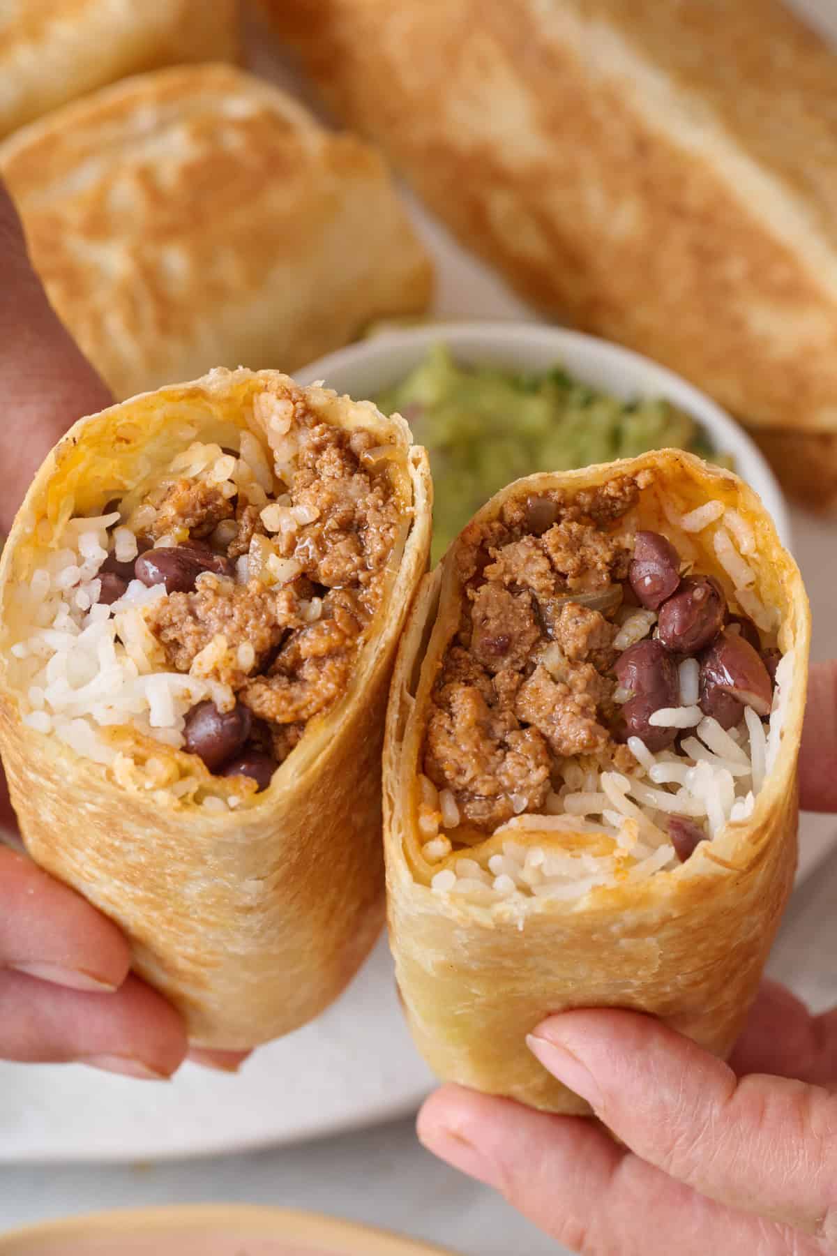A halved grown beef burrito with black beans and rice.