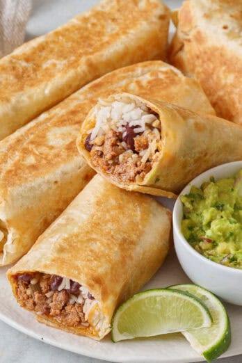 Seasoned ground beef burritos on a plate with a side of guacamole.