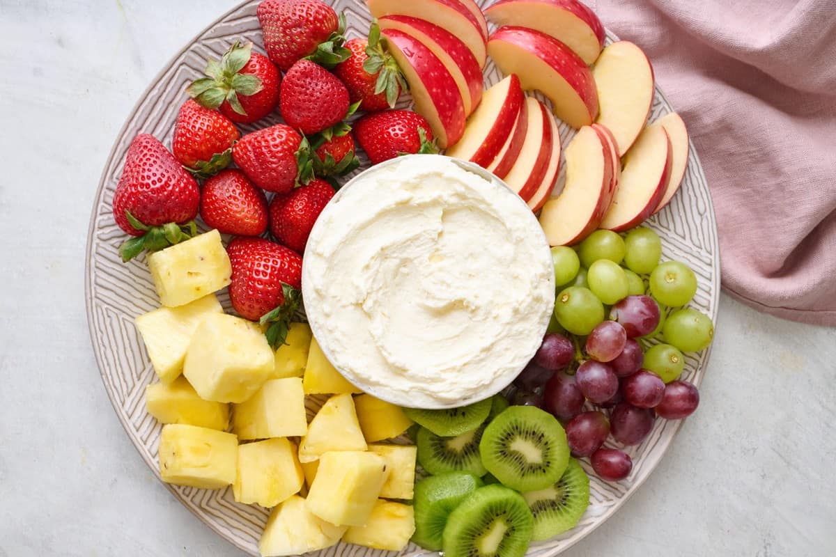 Cream cheese Dip in a bowl on a round platter with fruit around for dipping.