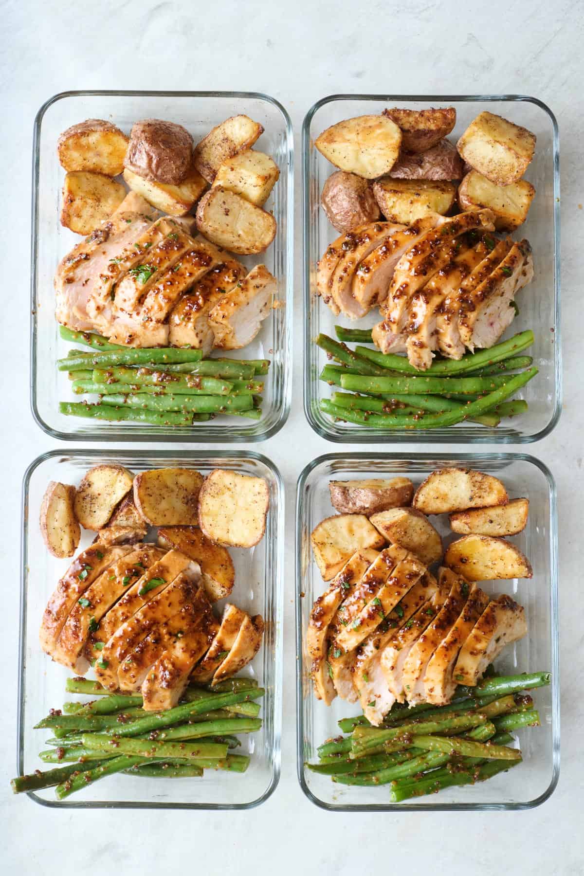 Four glass containers filled with sliced chicken, roasted potatoes, and green beans.