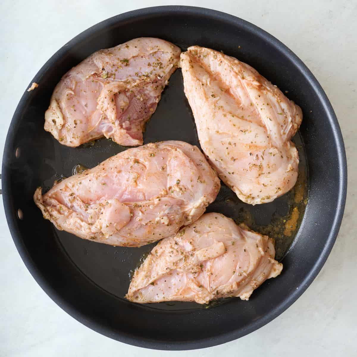 Marinated chicken breast in a skillet before cooking.