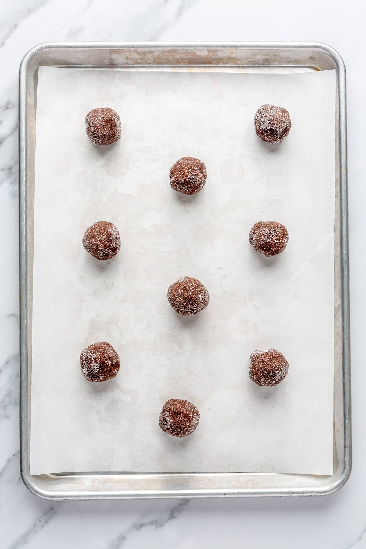 Tray of sugar coated cookie dough balls on a parchment lined baking sheet before baking.