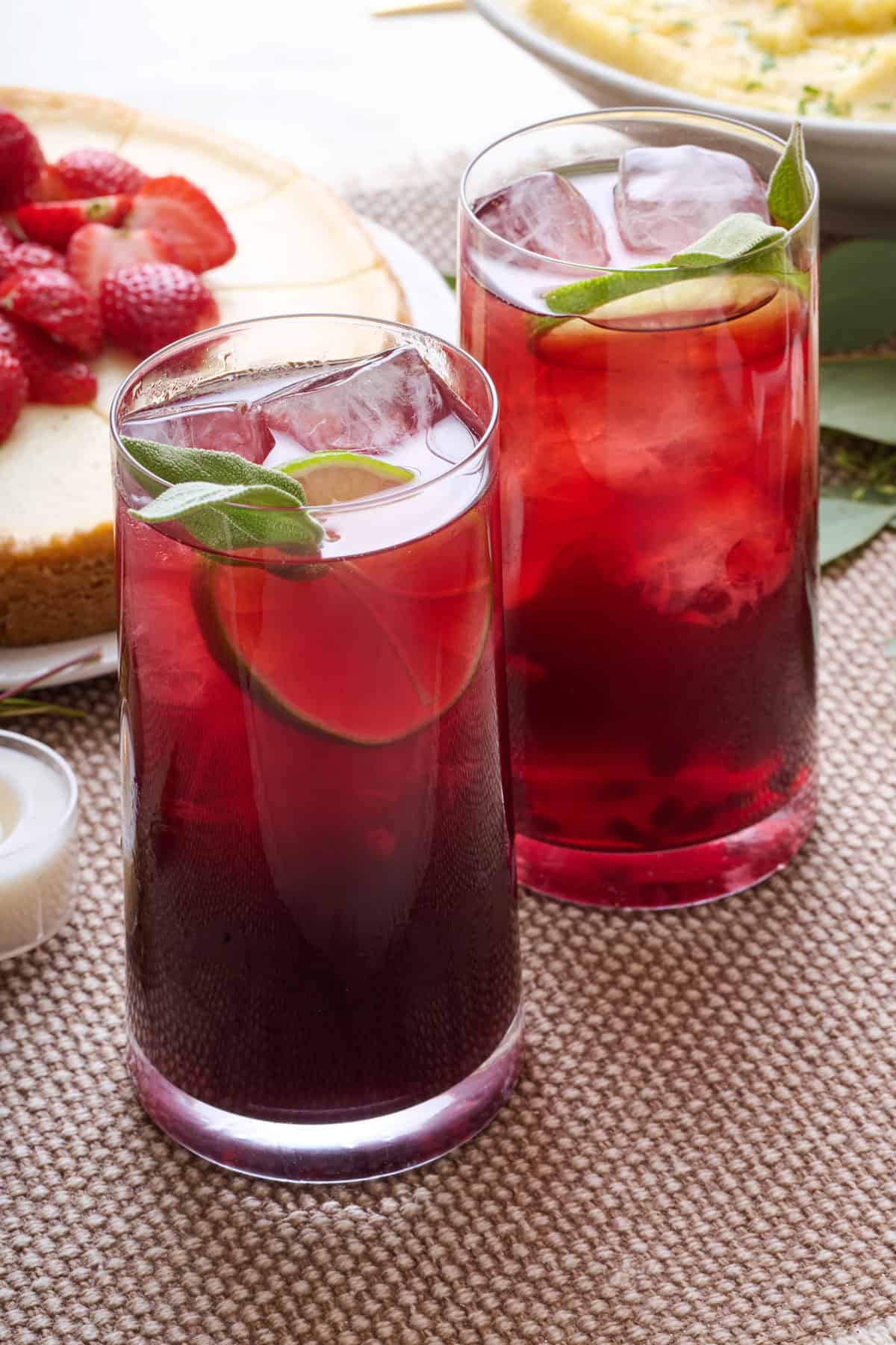 Two glasses of pomegranate mocktail with a lime slice tucked into glass and fresh sage leaf on top.