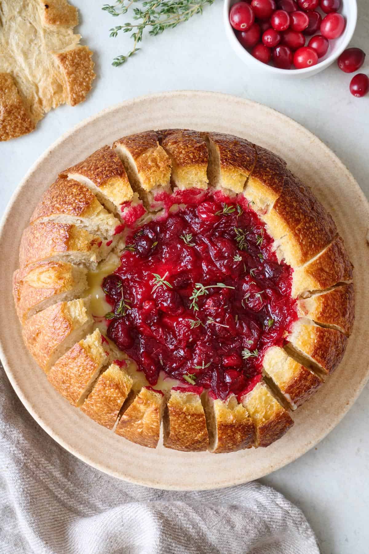 Cranberry baked brie in bread on a platter with fresh cranberries nearby.