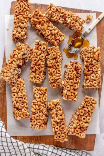 Honey Nut Cereal bars on parchment paper/cutting board after cutting into 12 pieces, spoon with honey resting on paper.