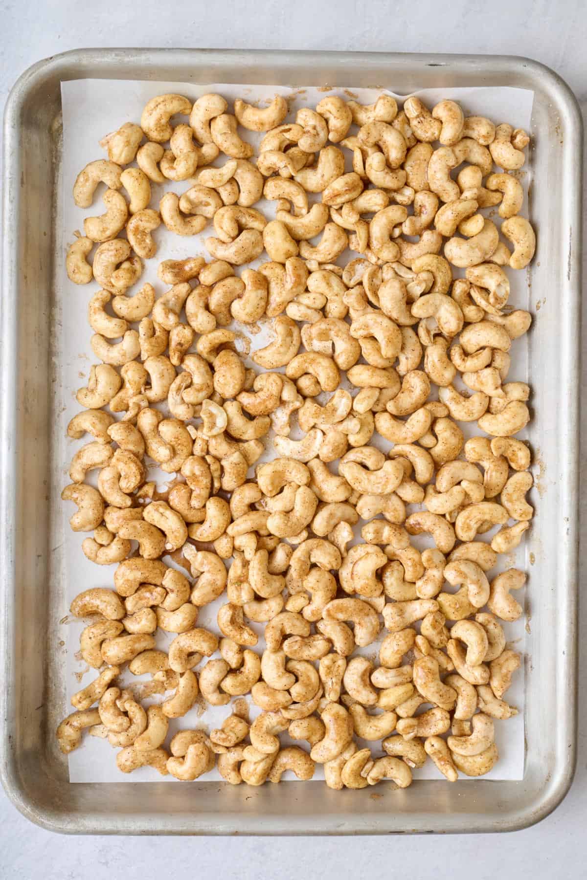 Coating raw nuts on a parchment line baking sheet.