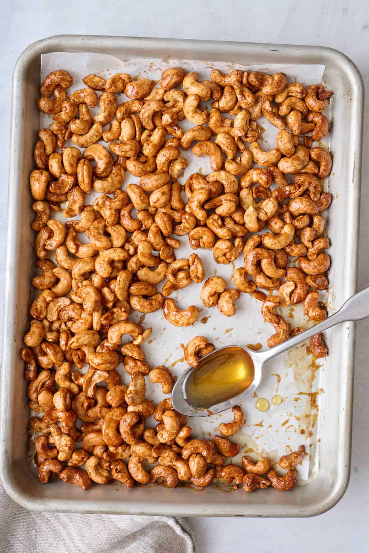 Honey roasted cashews on a baking sheet with a spoonful of honey resting on pan.