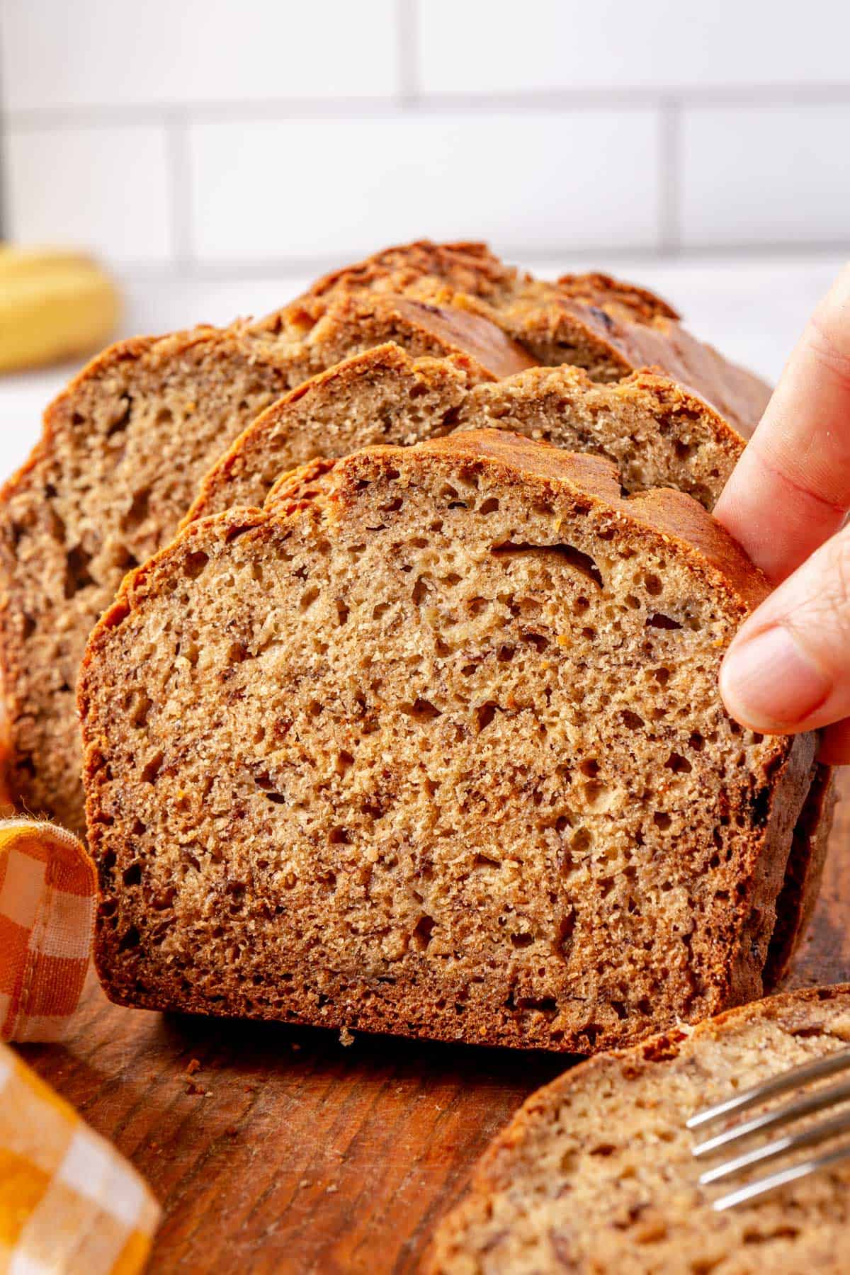Hand grabbing a slice of banana bread from cutting board.