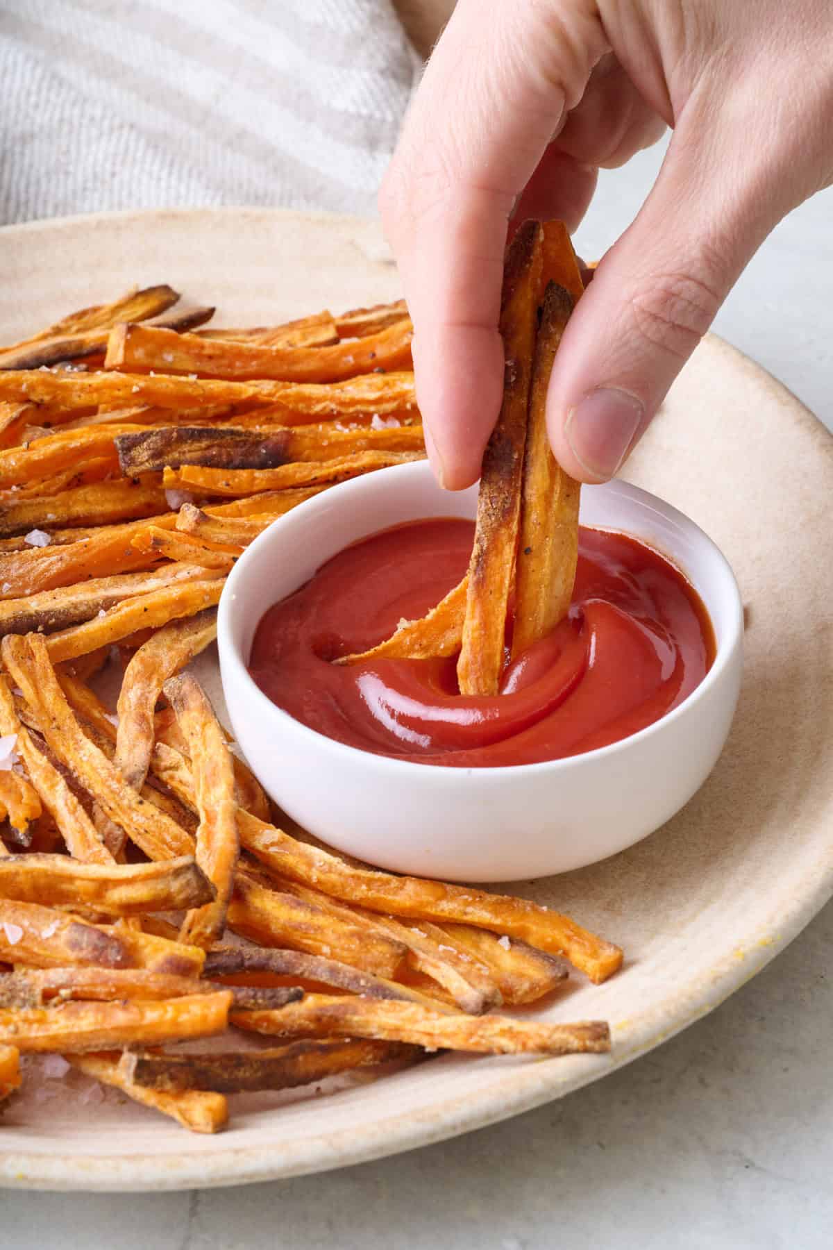 Hand dipping a few crispy sweet potato fries into ketchup.