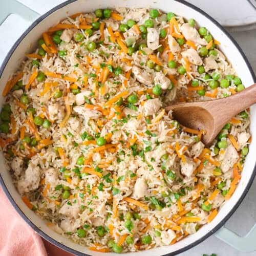 Cooked one pot chicken and rice in a pan being fluffed with a wooden spoon after cooking.